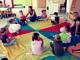 Dzieci z wychowawczynią siedzą na wielokolorowej, okrągłej płachcie
