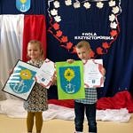 Dziewczynka i chłopiec prezentują wykonane własnoręcznie herby gminy Wola Krzysztoporska