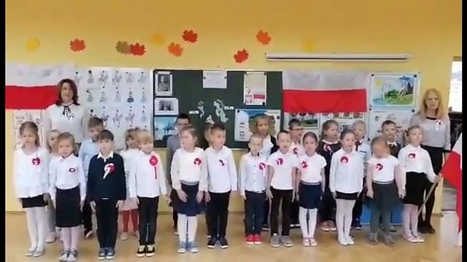 Maluchy ubrane w galowe stroje z kotylionami śpiewają hymn narodowy