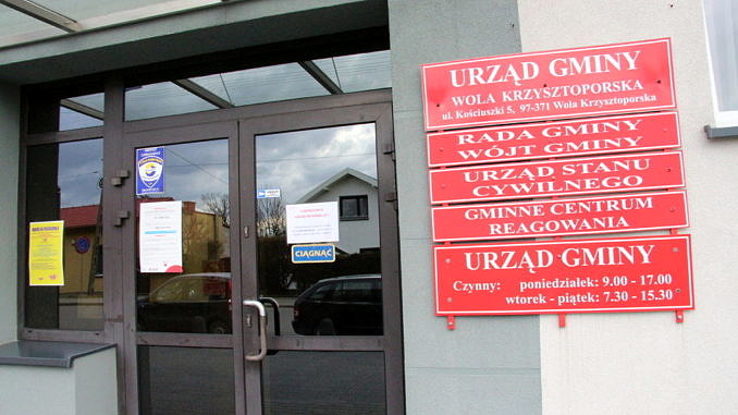 Drzwi do Urzędu Gminy w Woli Krzysztoporskiej, obok czerwone tablice informacyjne