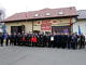 Członkowie jednostki OSP Parzniewice w mundurach (także członkowie drużyny młodzieżowej w czerwonych dresach) stoja przed budynkiem OSP Parzniewice