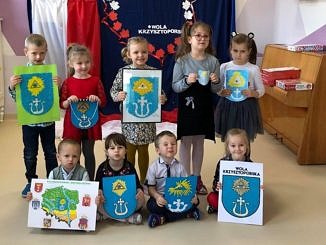 Grupa przedszkolaków prezentuje wykonane własnoręcznie herby gminy Wola Krzysztoporska