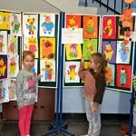 Dzieci pokazują kolorową wystawę rysunków, których głównym bohaterem jest miś