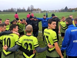 Grupa piłkarzy LKS Wola Krzysztoporska w seledynowych koszulkach razem z trenerem stoi w kręgu; piłkarze trzymają się za ramiona