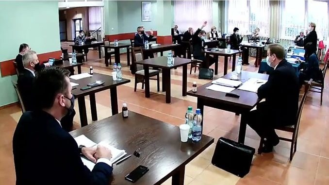 Sesja Rady Gminy Wola Krzysztoporska. Radni i władze gminy siedzą przy oddzielnych stolikach w maseczkach