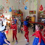 Grupa dzieci w przebierańcowych strojach bawi się na sali udekorowanej balonami i serpentyną