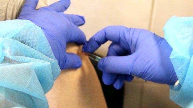 osoba w niebieskich rękawiczkach podaje szczepionkę w ramię