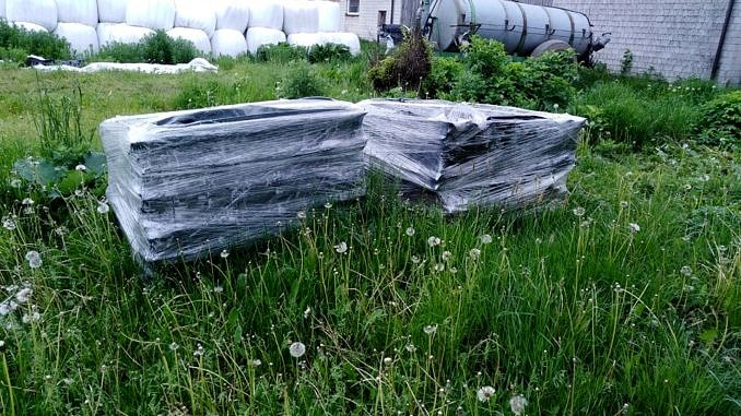 Azbest - tzw. eternit owinięty folią, składowany na paletach, na trawie