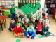 Grupa dzieci przedszkolnych siedzi na podłodze z zielonymi opaskami z dinozaurami na głowach