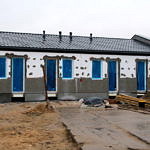 Budynki komunalne w budowie - białe budynki pokryte dachem; otwory na okna i drzwi zasłonięte niebieską folią
