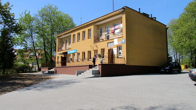 Ośrodek zdrowia Parzniewice Żółty piętrowy budynek ze schodami i podestem, a przed nim utwardzony kostką plc - prking