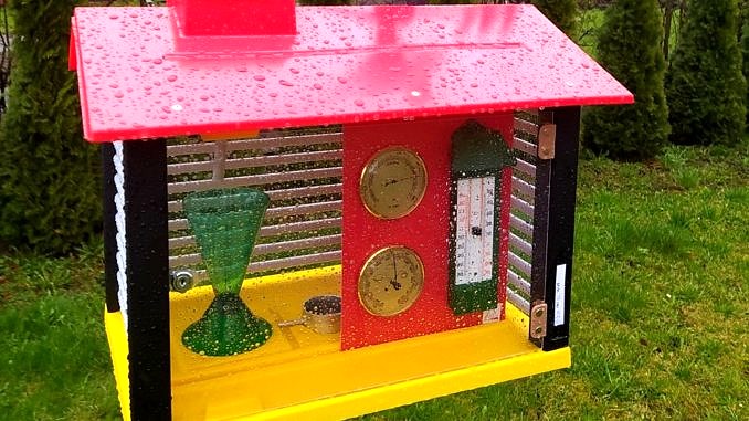 Stacja meteorologiczna - kolorowa skrzynka ze spadzistym czerwonym daszkiem i żółtą podłogą, a w środku urzadzenia do pomiaru pogody; nad daszkiem zamontowany Kur (kogut) do pomiaru kierunku wiatru