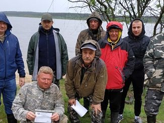 Grupa wędkarzy (część z dyplomami) nad zbiornikiem wodnym
