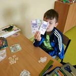 Dziecko nad stołem z banknotami i wyciętymi z papieru monetami