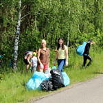 Ludzie sprzątający teren przy drodze i fragment lasu
