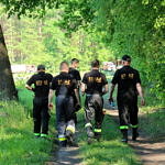 Strażacy w czarnych koszulkach id drogą leśną