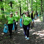 Grupa ludzi (część w zielonych koszulkach Leszy) sprząta las