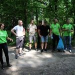 Grupa ludzi (część w zielonych koszulkach z napisem Leszy, z niebieskimi workami przygotowuje się do wyjścia do lasu