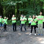 Grupa ludzi (część w zielonych koszulkach z napisem Leszy, z niebieskimi workami przygotowuje się do wyjścia do lasu