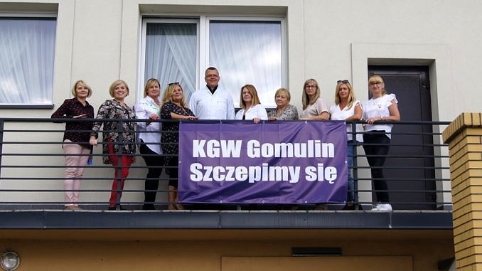 Na balkonie budynku członkinie KGW - przed nimi zawieszony baner KGW Gomulin szczepimy się