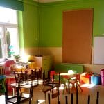 Kolorowa klasa szkolna po odmalowaniu ścian na zielono; ławki szkolne i zawieszone na nich krzesełka