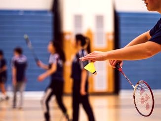 Badminton - na pierwszym planie dłoń z lotką, w tle zawodnicy