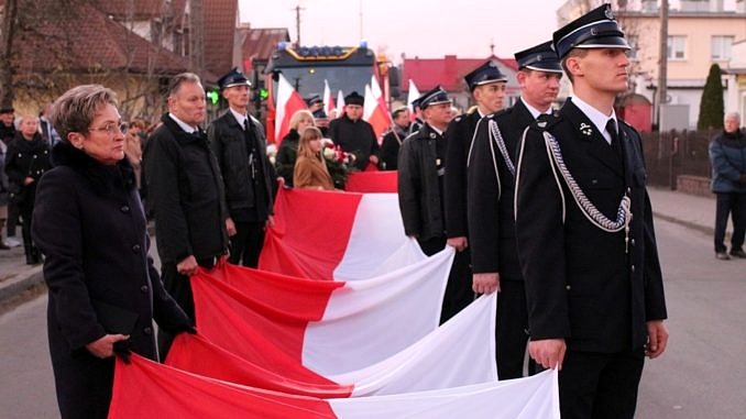 ludzie trzymający wielką biało-czerwoną flagę; m.in. strażacy