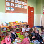 Dzieci siedzą na macie przy regale z ksiązkami i przeglądają książki