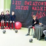 Uczniowie w czarnych strojach z czerwonymi kokardkami podczas montażu na temat AIDS/HIV