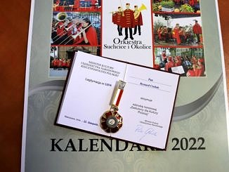 Legitymacja z medalm na kalendarzu z orkiestrą z Suchcic