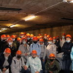 Grupa osób w strojch ochronnych i pomarańczowych kaskach podczas wycieczki w kopalni