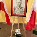 Rysowany portret Ludwika Czyżewskiego stoi na stojaku; obok baiło-czerwone flagi