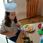 dziewczynka w kucharskiej czapce przy krojeniu owoców