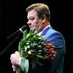 Wójt Roman Drozdeknprzy mikrofonie z naręczem tulipanów