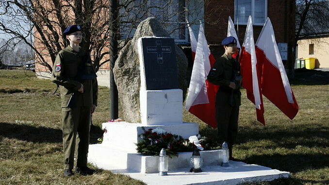 Apel Pamięci - chłopcy w mundurach stoja przy obelisku w Bujnach w tle flagi