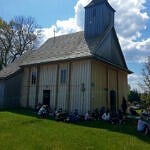 uczestnicy rajdu siedzą na trawie pod kościołem w Postękalicach
