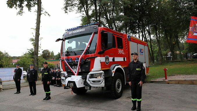 Strażacy stoją przy nowym, udekorowanym wstążkami wozie bojowym